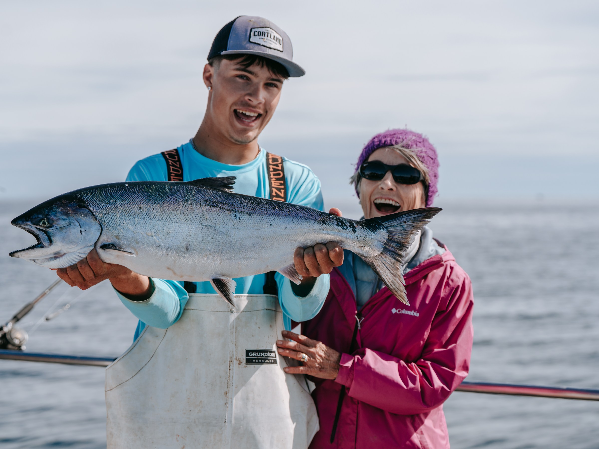 Two people on a boat holding a large fish, both smiling.
