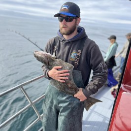 Person in cap and sunglasses holding a large fish on a boat.