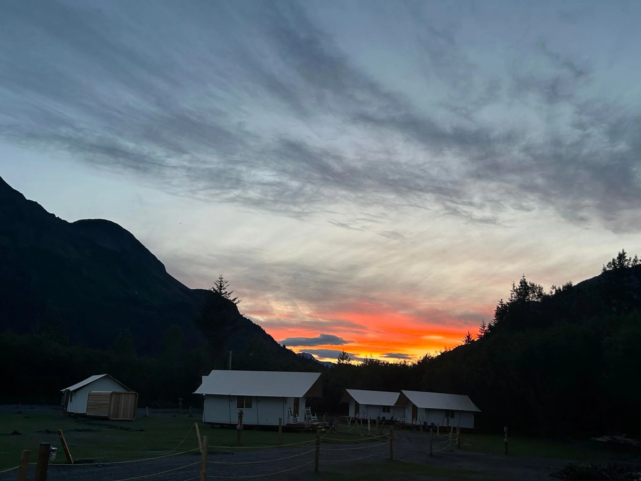 Sunset sky over mountains and cabins with vibrant orange and blue hues.