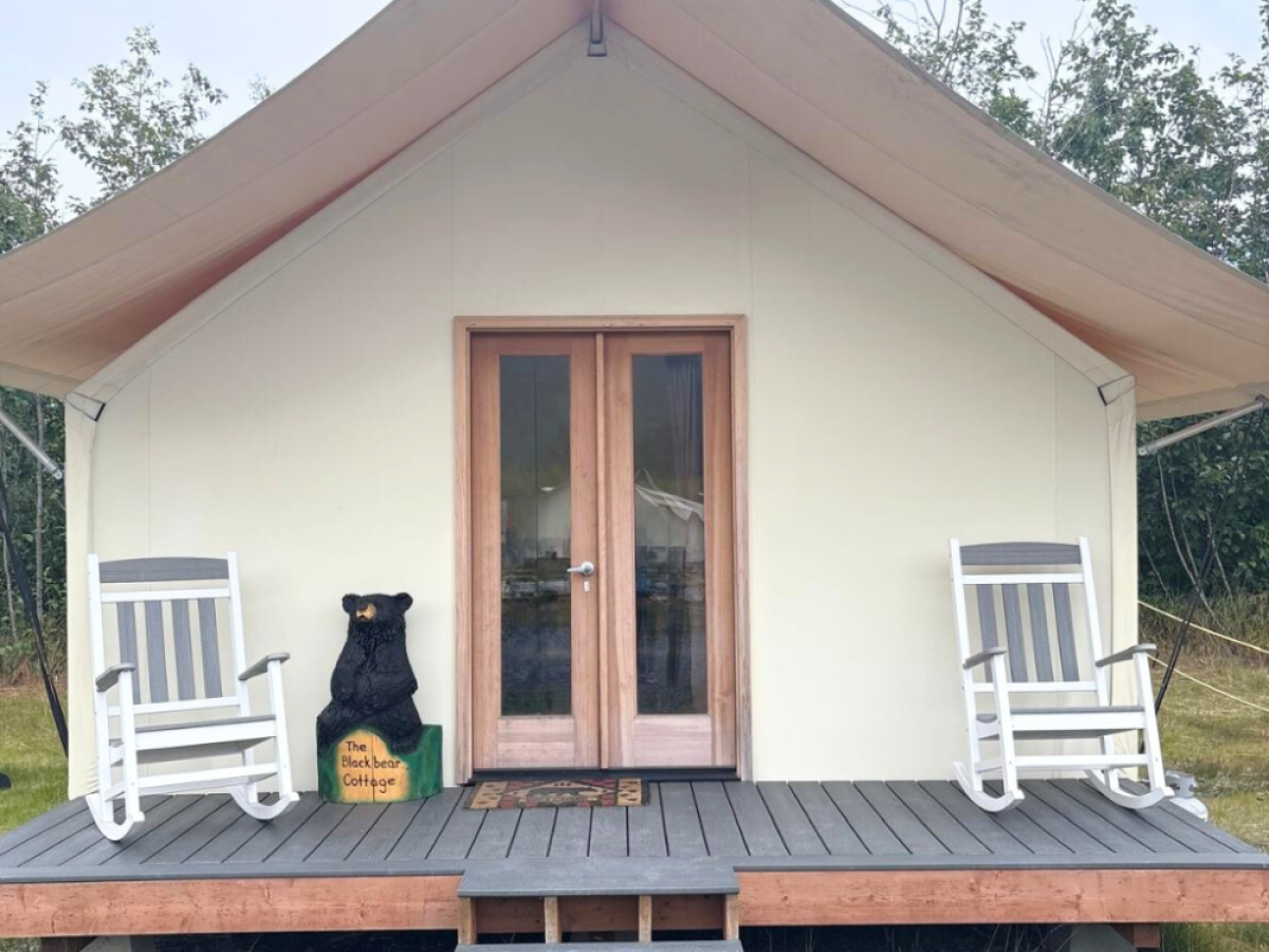 Tent with porch, two rocking chairs, and bear statue in outdoor setting.