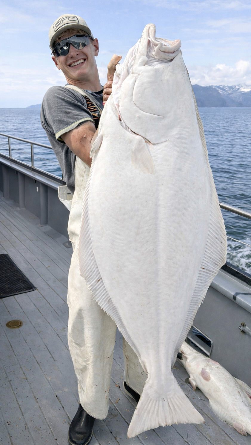 Person on a boat holding a large white fish with a mountainous background.